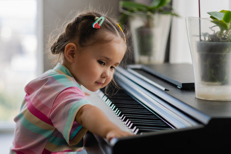 A beautiful little asian girl plays the piano in the living room or music school. Preschool child having fun learning to play a musical instrument. The concept of education, skills.の写真素材