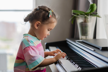 Side view of cute asian girl playing piano at home. Preschool child learning to play music instrument. Education, skills concept.の写真素材