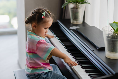Little Asian girl playing synthesizer and looking at the camera. Preschool child learning to play music instrument. Education, skills concept. happy childhoodの写真素材
