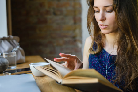 Attractive young girl reading a book while having breakfast in a coffee shop. close-up.の写真素材