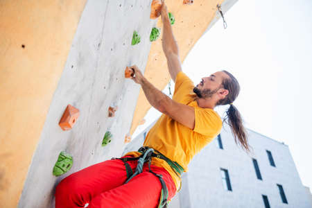 Man climber on artificial climbing wall outdoors against the background of an office building.の写真素材