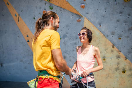 A man helps a young woman to put on her climbing equipment against the backdrop of a climbing wall outdoors.の写真素材