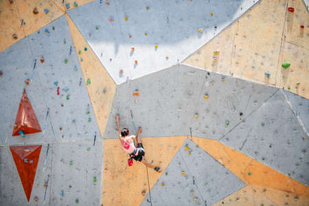 Sportswoman climber moving up on steep rock, climbing on artificial wall. Extreme sports and bouldering conceptの写真素材