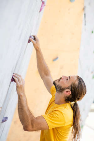 A sporty man in a yellow t-shirt climbs an climbing wall.の写真素材