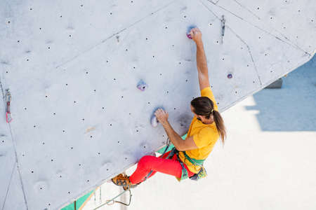 Sportsman climber moving up on steep rock, climbing on outdoor artificial wall. top view.