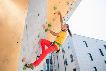 Man climber on artificial climbing wall outdoors against the background of an office building.