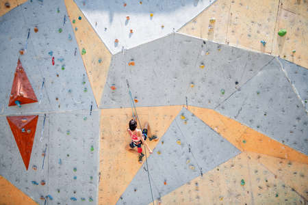 Sportswoman climber moving up on steep rock, climbing on artificial wall. Extreme sports and bouldering conceptの写真素材