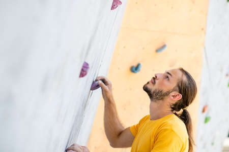 A sporty man in a yellow t-shirt climbs an climbing wall.の写真素材