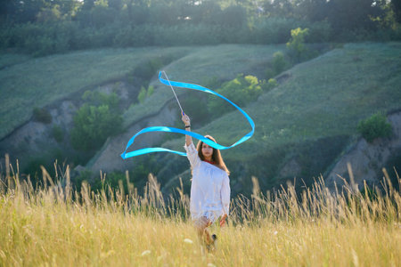 A teenage girl with a gymnastic ribbon on a hillside. girl on the background of bayrak. Tall dry wild grass.の写真素材