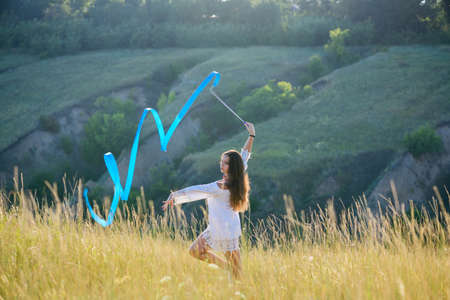 A teenage girl with a gymnastic ribbon on a hillside. girl on the background of bayrak. Tall dry wild grass.の写真素材