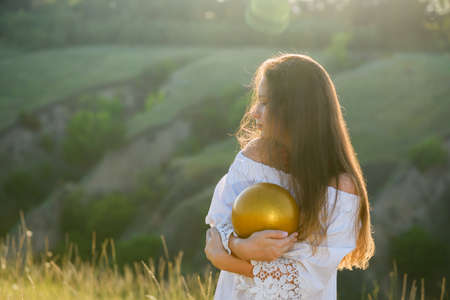 Teenage girl with a gymnastic ball on the background of a ravine. Sunset backlight.の写真素材