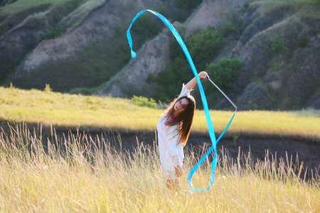 A teenage girl with a gymnastic ribbon on a hillside. girl on the background of bayrak. Tall dry wild grass.の写真素材