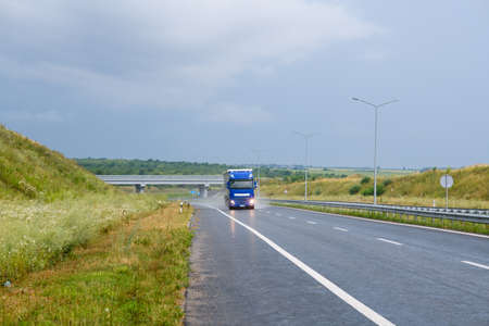Big blue truck with roof spoiler transporting commercial cargo in semi trailer running on the evening wet glossy slippery road with raining weatherの写真素材