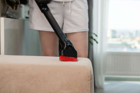 Woman vacuuming sofa. Sofa cleaning with vacuum cleaner. Home cleaning background. Dust cleaning in the house.の写真素材