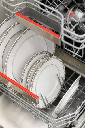 Open dishwasher with clean dishes in a white kitchen. Clean plates, cups and dishes. Nobody. selective focus.の写真素材