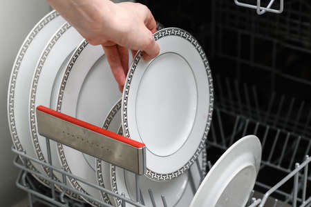 The female hand takes out a clean plate from the dishwasher. Clean dishes in the dishwasher close-up. top view.の写真素材