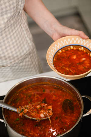 A woman pours freshly prepared Ukrainian borscht into a traditional earthenware bowl.の写真素材