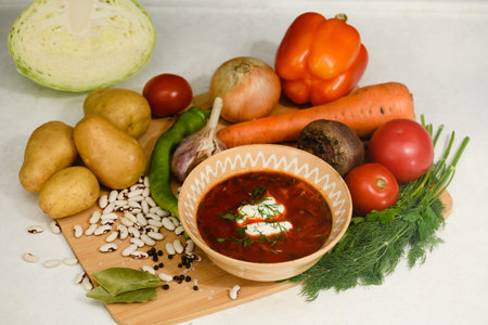 Traditional Ukrainian borscht with sour cream in a clay bowl. Ingredients for cooking borscht on a wooden cutting board.の写真素材