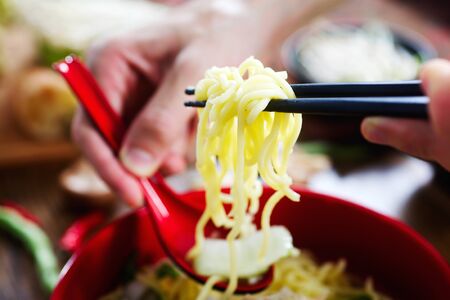 Chopsticks holding noodles under bowl. Closeup photo