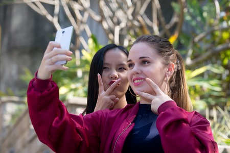 Two young beauty girlfriends doing selfie outdoorの写真素材