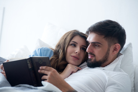 Young couple together reading a book lying in bedの写真素材