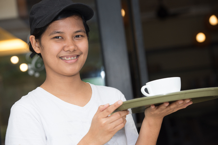 Young waiter holding a tray with a glass of coffeeの写真素材