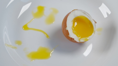 Soft-boiled egg is broken on a white plate closeup photo