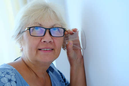 Mature woman overhears neighbors through the wallの写真素材