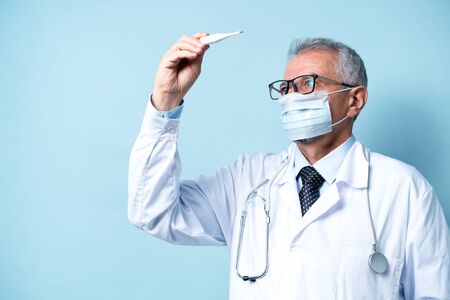 Senior doctor in glasses and a mask checks the temperature of the patientの写真素材