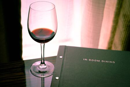A glass of wine and a dinner menu on the background of a window and curtains