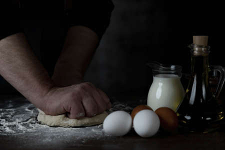 Baking fresh bread in the bakery, hands of male knead dough on kitchen table with flourの写真素材