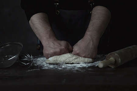 Baking fresh bread in the bakery, hands of male knead dough on kitchen table with flourの写真素材