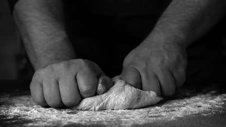 Baking fresh bread in the bakery, hands of male knead dough on kitchen table with flourの写真素材