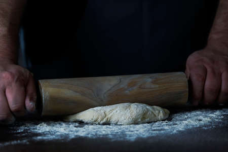 Man Baker or chef is rolling fresh dough with a dough roller on a wooden surface.の写真素材