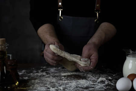 Baking fresh bread in the bakery, hands of male knead dough on kitchen table with flourの写真素材