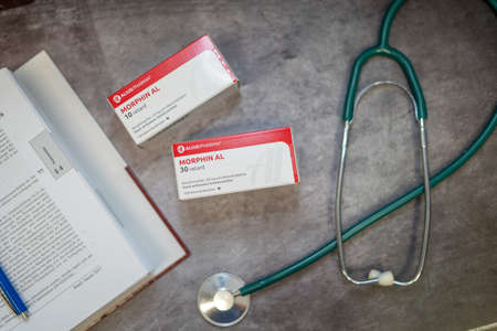 Drug box of  Morphine,pain medication of the opiate.On a table and in the background a medical book.