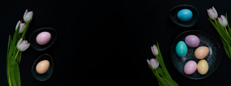 Tulip flowers and pastel colored Easter eggs in a dark granite plate against Black background.