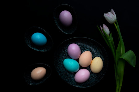 Tulip flowers and pastel colored Easter eggs in a dark granite plate against Black background.の写真素材