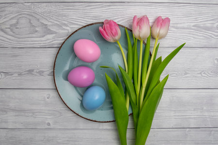 Easter eggs in blue ,pink and three tulips on a blue plate and white colored wooden tableの写真素材