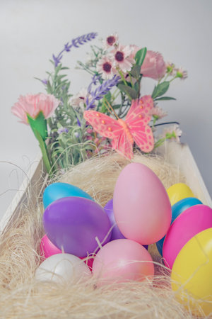 Colored Easter eggs and flowers in wooden white box with pink butterfly  on white background .