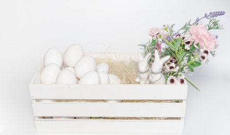 White colored heart in front and white eggs and blurred flowers in the background Easter or food...