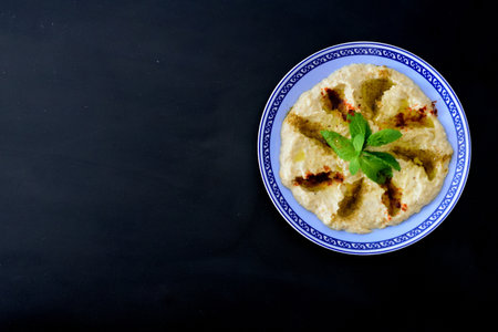 Hummus bowl with blue edge, decorated with herbs and olive oil over a black wood background.の写真素材