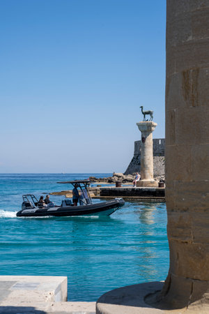 tourists boat  sailing into Mandraki  harbor passing the Doe statues in Rhodes harbor.のeditorial素材