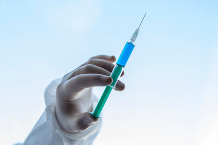 Syringe for injection, Doctor wearing surgical gloves holding a needle or syringe for injection with a blue liquid against white blue background.の写真素材