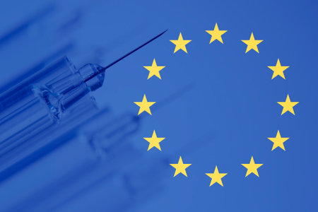 Vaccination syringe in focus and behind several not focused and background the European Union flag.の写真素材