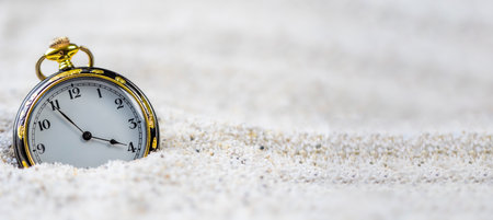 Antique watch, vintage old black and gold watch in the sand in daylight.
