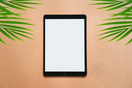 Tablet computer with blank screen on beige background with palm leaves.