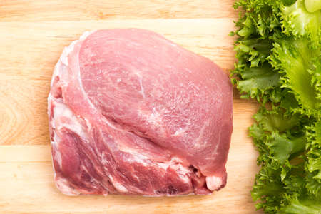 salad greens and uncooked pork on chopping blockの写真素材