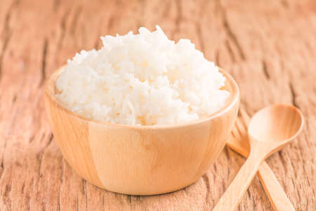 Steamed jasmine rice in a bowl with spoon on wood backgroundの写真素材