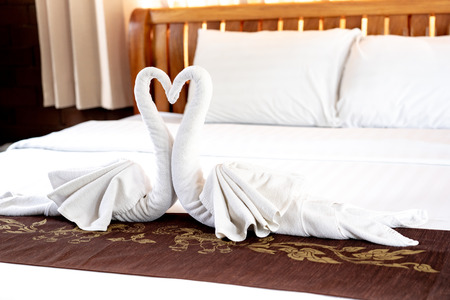 Towels folded in couple of swan shape with heads in heart shape on bed at the resortの写真素材